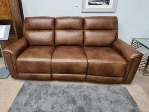 Brown leather sofa in a living room setting with a bookshelf and framed picture on the wall.