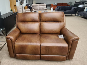 Brown leather sofa in a showroom setting with other furniture in the background.
